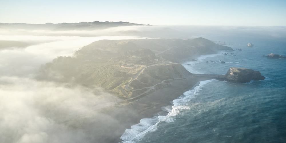 A headland from the air, sea fog rolling in across it