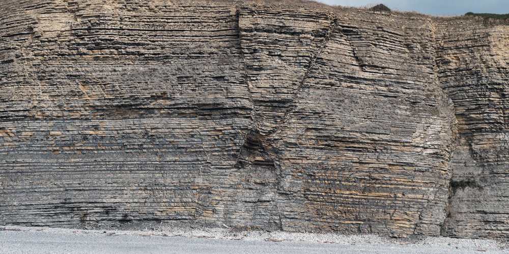 A cliff face of stacked sediment, the lower layers only visible where it has broken away