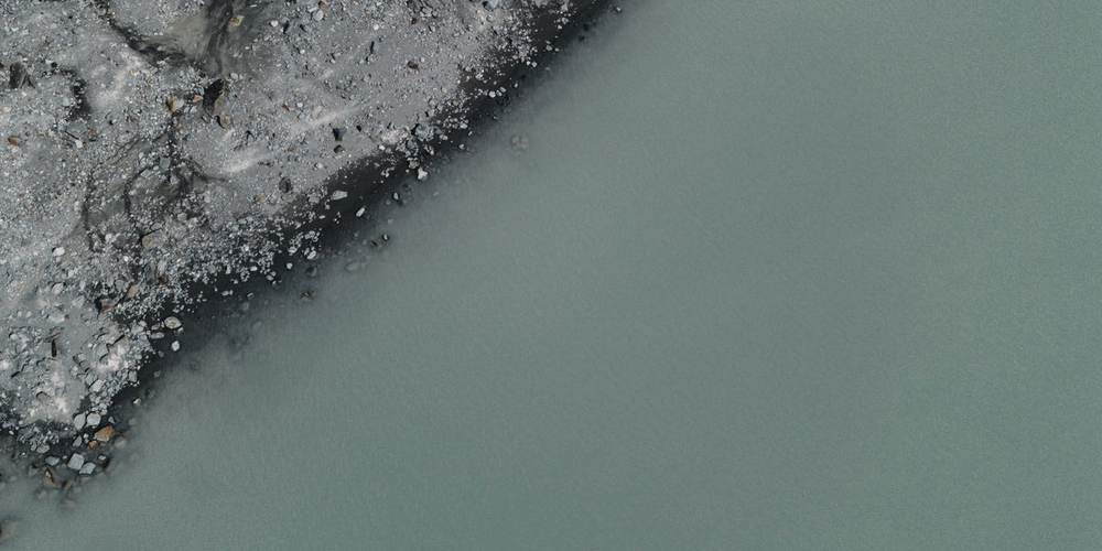 The edge where stony ground meets still green water, seen from above